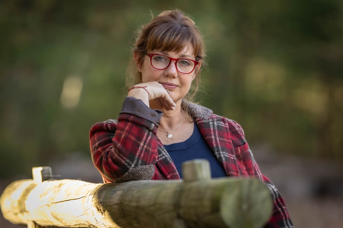 Professional Headshots in CT | Professional therapist leans on horse tie post wearing read glasses.