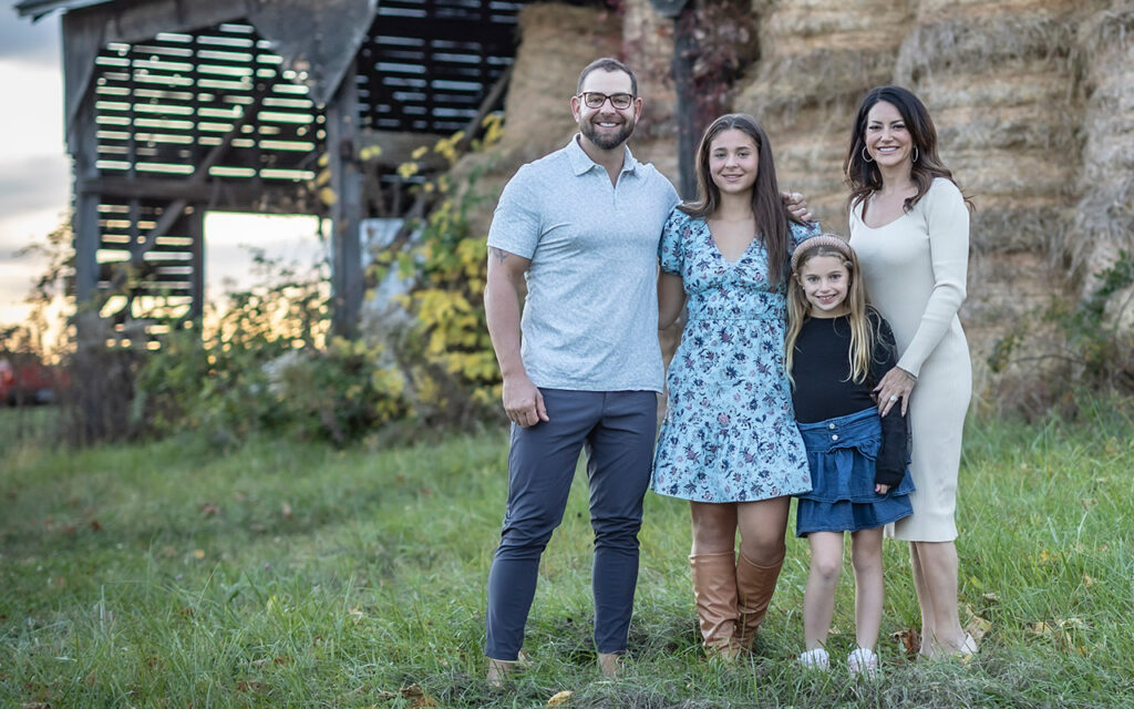 Photographer in Avon | Rob Faber Photography | Outdoor family portrait of four standing in front of a rustic barn, captured in natural evening light for a timeless fine-art look.