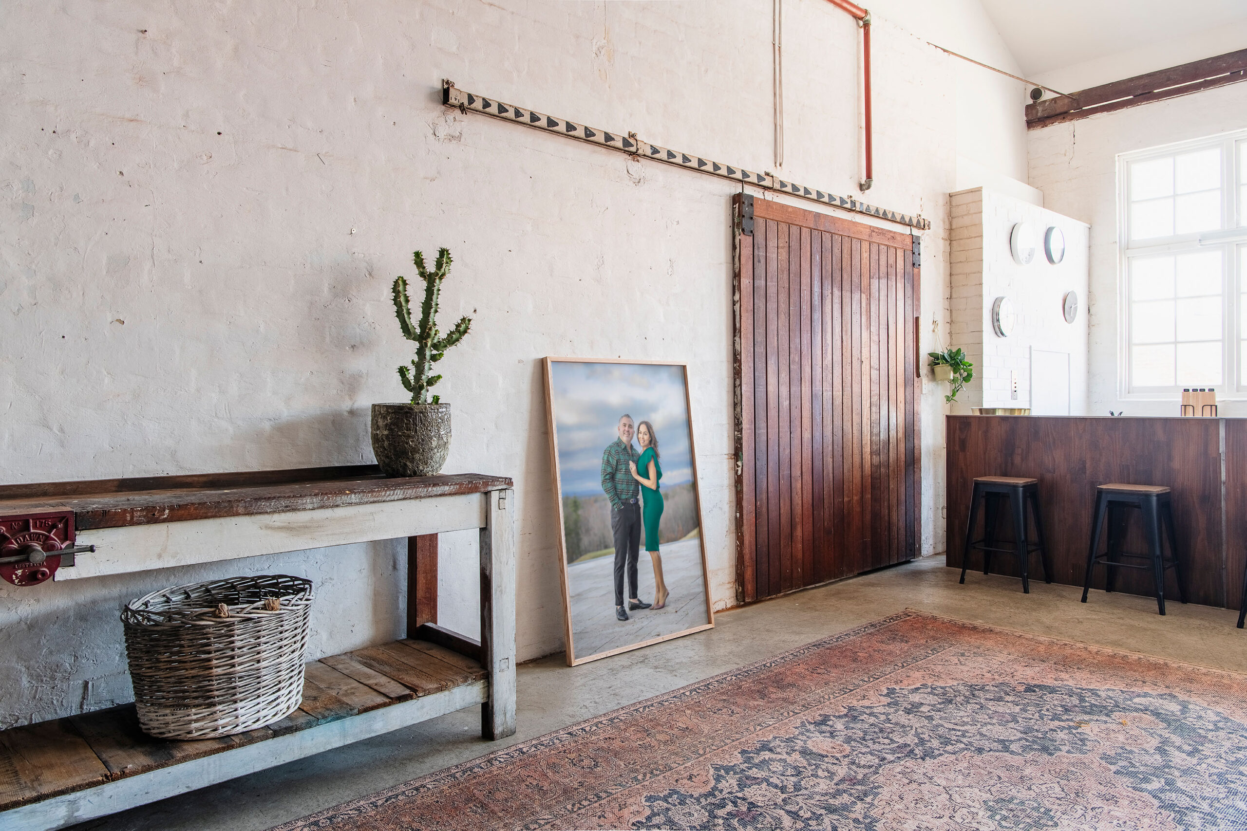 Photographer in CT | CT photographer | Family Photos near Suffield- Framed wall art portrait of a couple leaning against a rustic wooden barn door in a modern studio space with vintage rugs, a cactus plant, and natural light.
