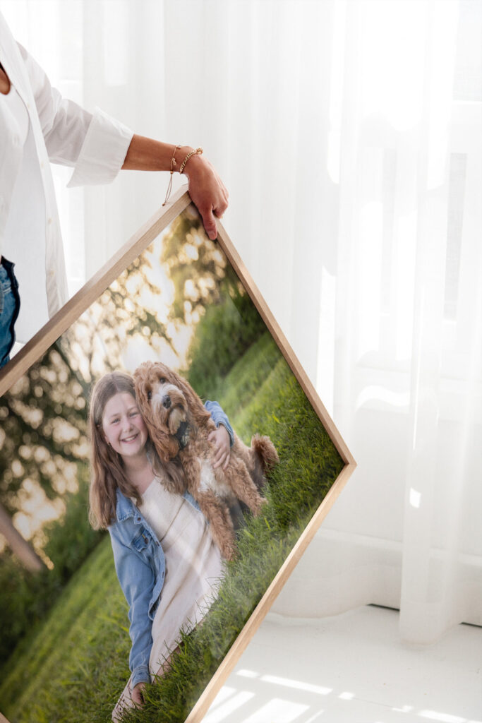 CT Photographer | A framed portrait of a young girl sitting in the grass with her golden doodle dog, photographed outdoors with warm evening light, being held by a client to display as fine art wall décor.