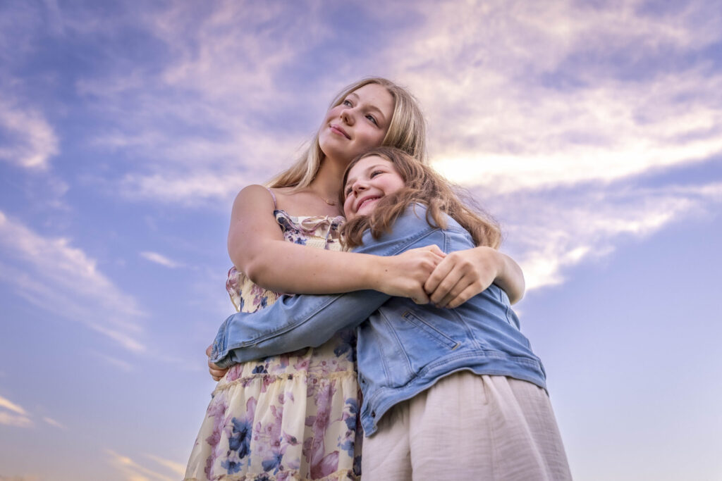 Simsbury Photographer | Two young girls stand embraced with a beautiful cloud filled pink sky.