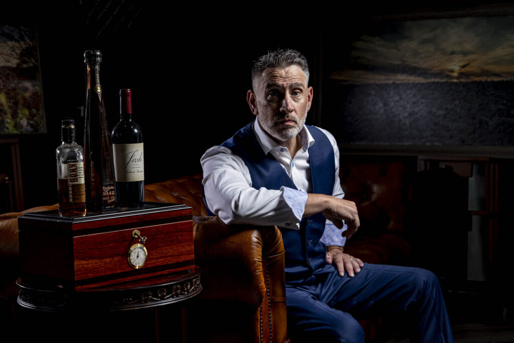 CT Photographer | Simsbury Photographer | Studio Photos. Rob Faber, dressed in blue suit vest and white shirt leans on leather chesterfield couch.