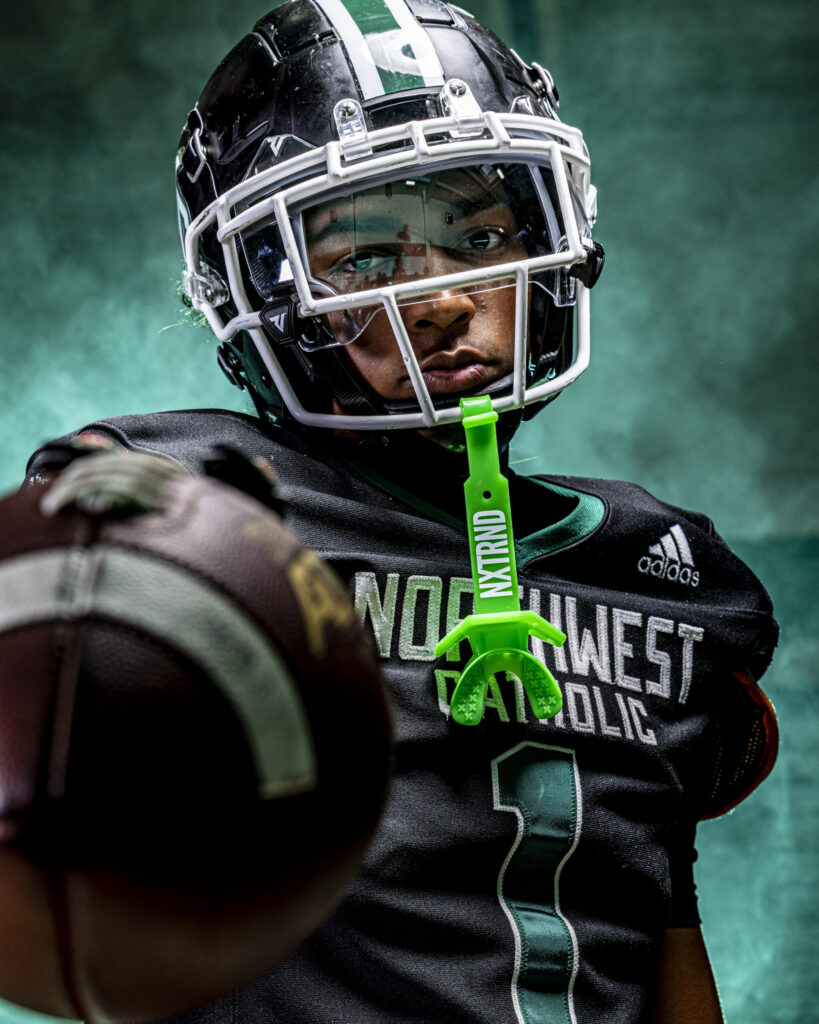 CT Sports Photographer | CT Photographer | Rob Faber Photography - Northwest Catholic football player in full gear points a football toward the camera with intensity, green smoke backdrop creating a bold and cinematic portrait.