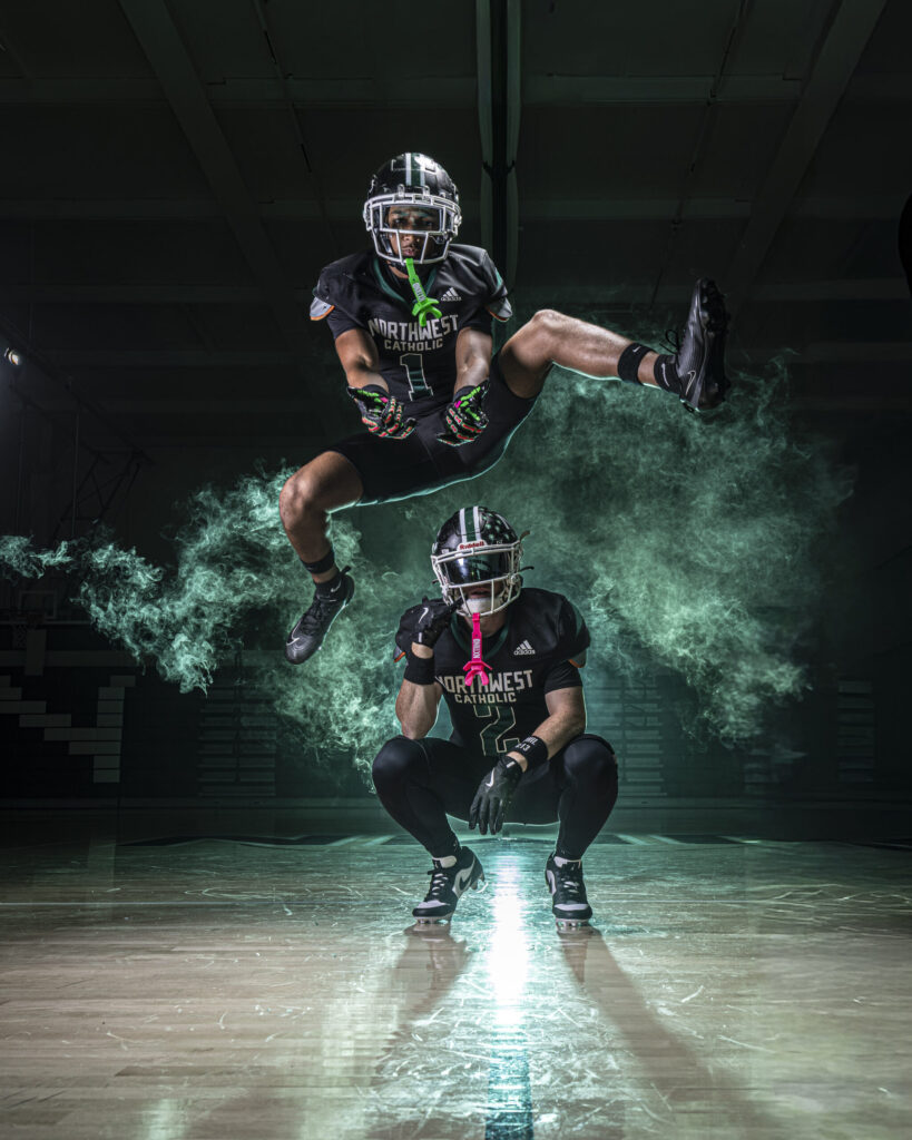 CT Sports Photographer | CT Photographer | Rob Faber Photography - Two Northwest Catholic football players in action pose, one leaping mid-air while the other crouches below, dramatic smoke and light creating a cinematic scene.