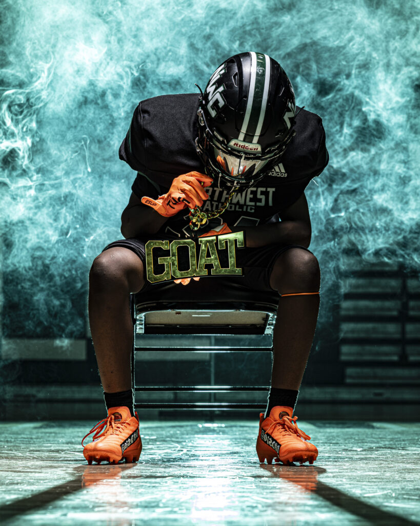 CT Sports Photographer | CT Photographer | Rob Faber Photography - Athlete sits on chair wearing football uniform and helmet, orange cleats, and GOAT chain, surrounded by teal smoke for a bold sports portrait.
