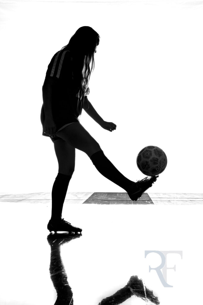 Photographer in West Hartford | Rob Faber Photography | Silhouette portrait of a female soccer player juggling a ball, captured with dramatic backlighting and reflection for a bold fine-art sports image.