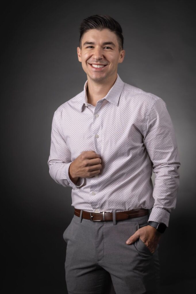 Modern business headshot of a smiling man in a light patterned shirt and gray pants, hands in pockets, photographed in studio by Rob Faber Photography.
