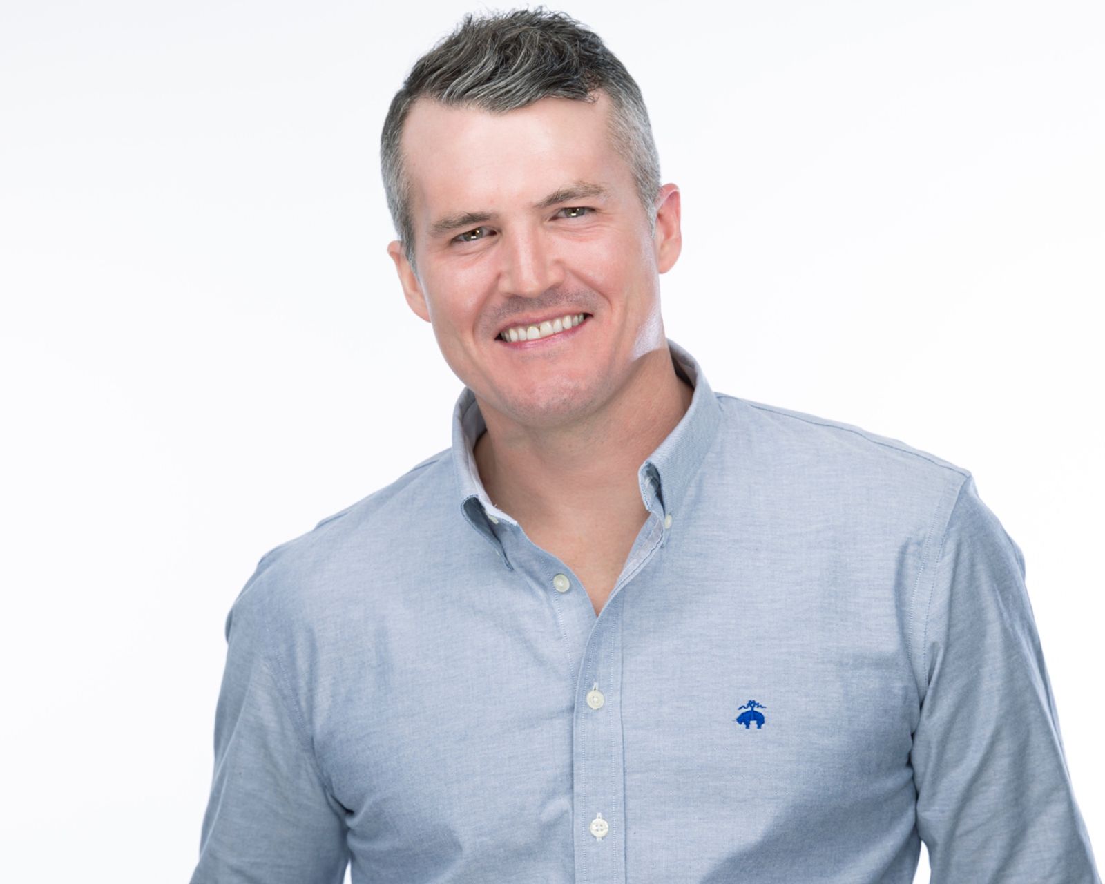Casual professional headshot of a smiling man in a light blue button-down shirt on a white background, captured by Connecticut photographer Rob Faber.