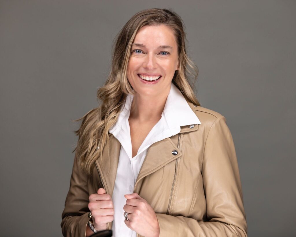 Bright, friendly portrait of a woman wearing a tan leather jacket and white blouse on a gray background, professional headshot by Rob Faber Photography.