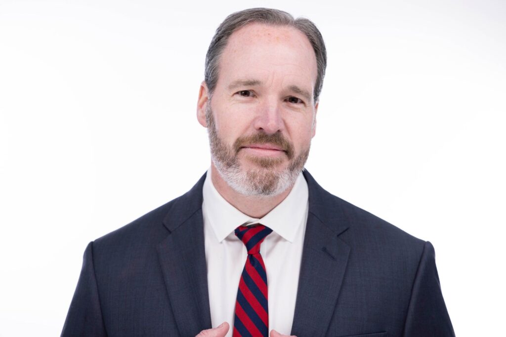 Professional headshot of a confident man in a dark suit and red striped tie on a white background, photographed by Rob Faber Photography in Connecticut.