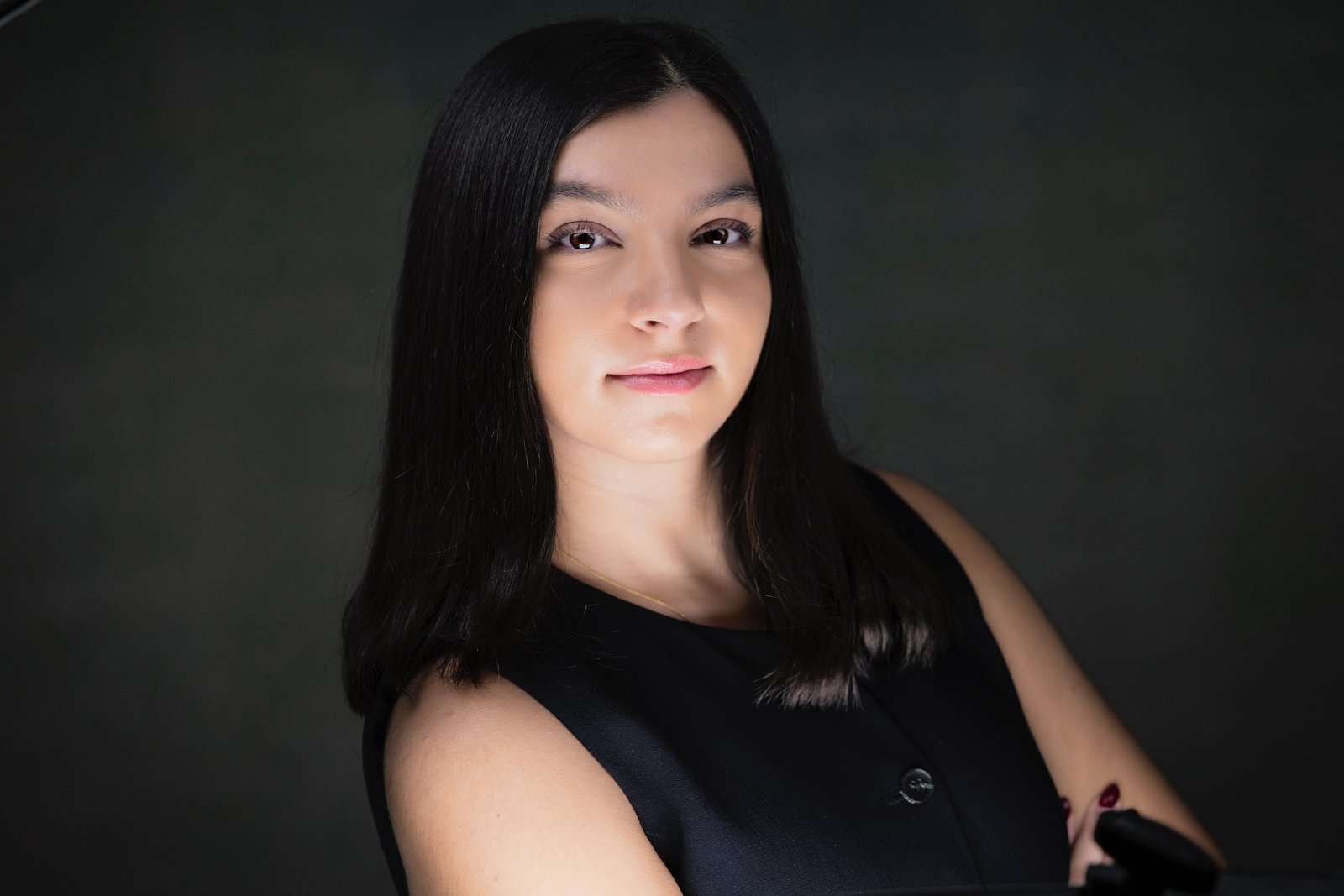 Rob Faber Photography | Headshot Photos | Professional headshot of a young woman with dark hair wearing a black sleeveless top, photographed in studio lighting against a dark background to convey confidence and professionalism.