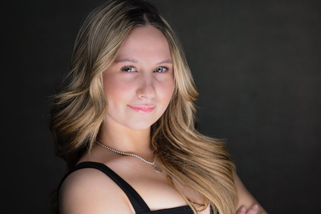 Rob Faber Photography | Headshot Photos | Professional headshot of a young woman with long blonde hair wearing a black sleeveless top, photographed in a studio setting with soft lighting for a polished, confident look.