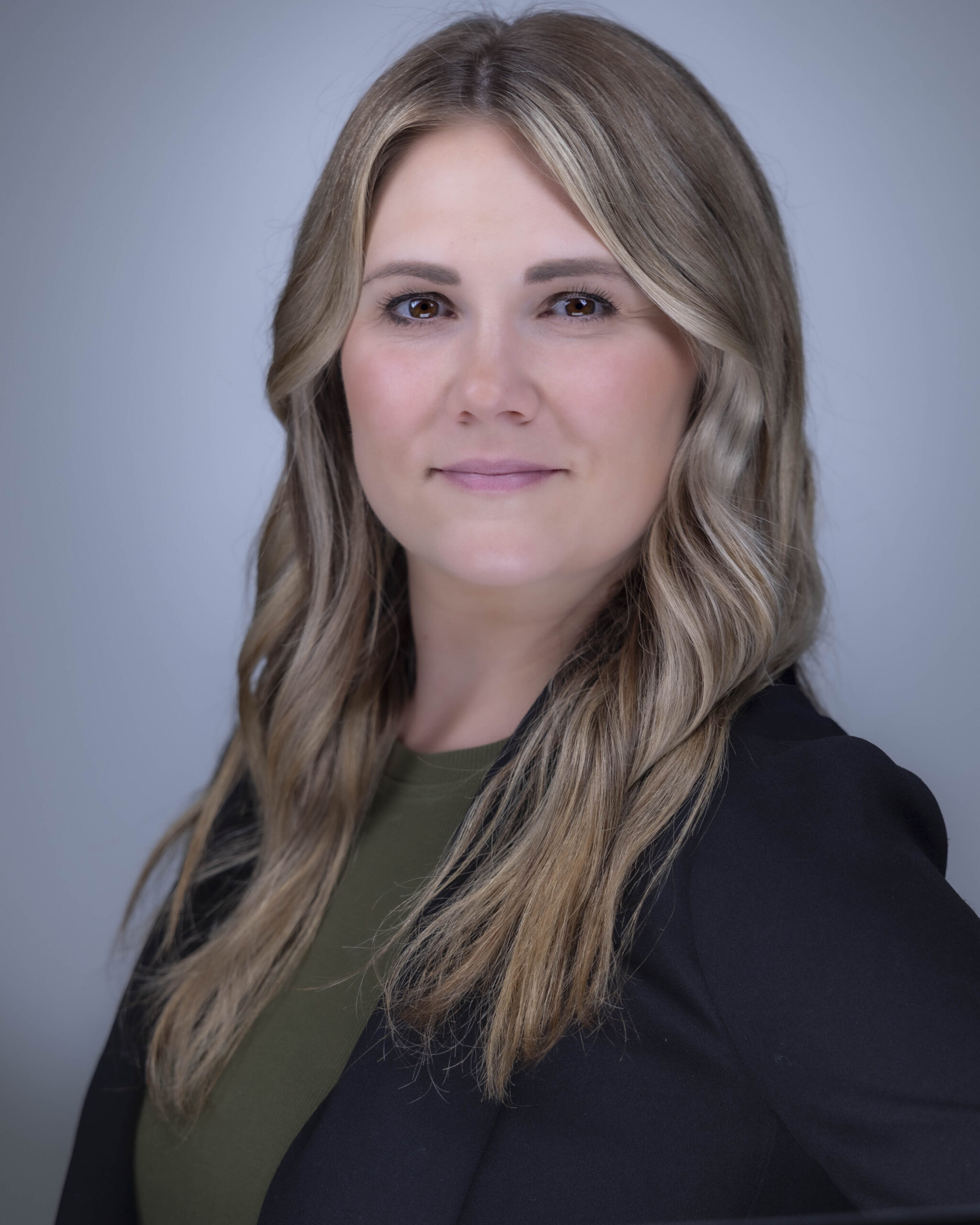 Rob Faber Photography | CT Photographer | Professional business headshot of a woman with long blonde highlighted hair wearing a black blazer and olive green top against a soft gray studio background, photographed with clean modern lighting for corporate branding and professional profile use.
