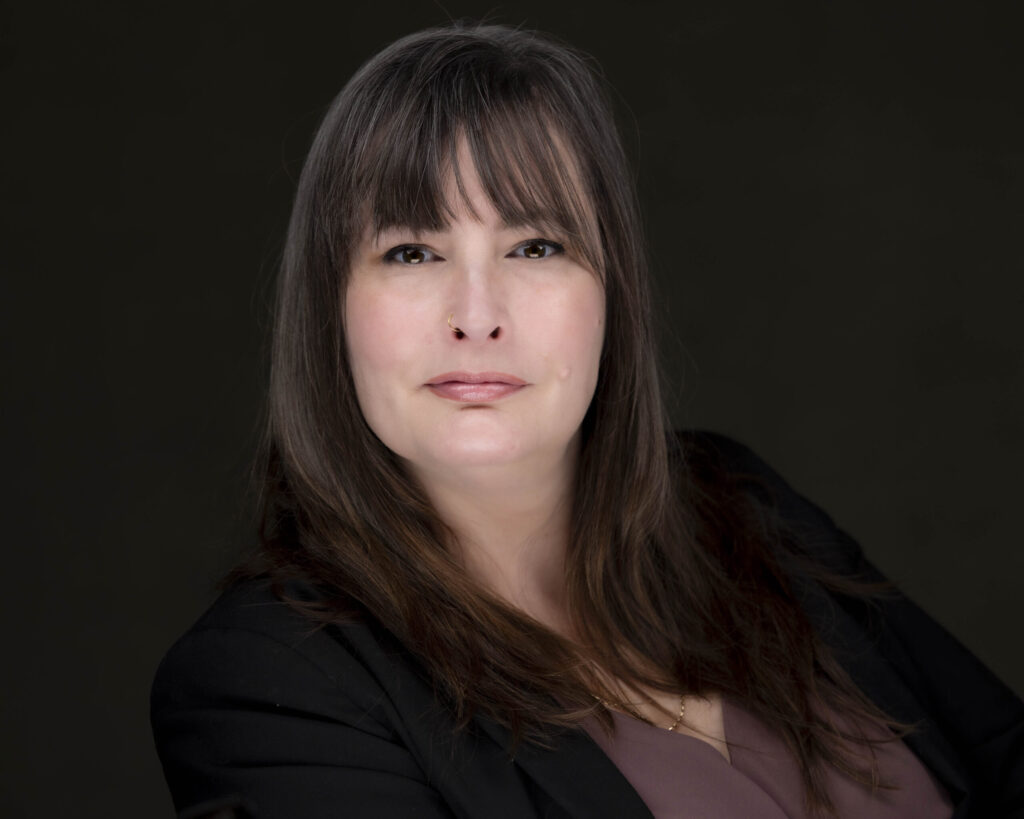 Rob Faber Photography | CT Headshot Photographer | Professional corporate headshot of a woman with long dark brown hair and bangs, wearing a black blazer over a mauve top. She is posed confidently against a dark studio background, looking directly at the camera with a calm, approachable expression. The dramatic lighting creates a polished, professional portrait ideal for business branding, executive profiles, LinkedIn, and corporate marketing materials.
