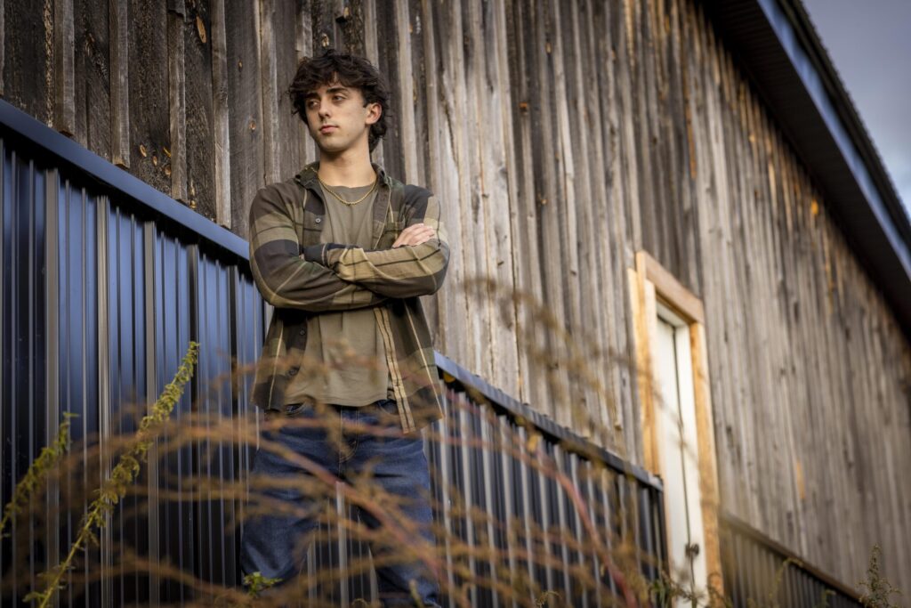 Rob Faber Photography | FBR Media | Senior Guys Portraits | Cinematic outdoor portrait of a senior guy standing on a staircase beside a weathered barn with dramatic natural light