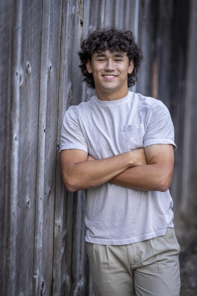 Rob Faber Photography | FBR Media | Senior Guys Portraits | Casual close-up portrait of a smiling senior guy standing against a weathered wooden wall during a Connecticut senior session
