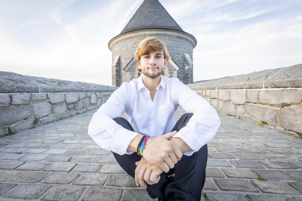 Rob Faber Photography | FBR Media | Senior Guys Portraits | Connecticut senior portrait of a high school guy sitting confidently in front of a castle-like stone structure during golden hour
