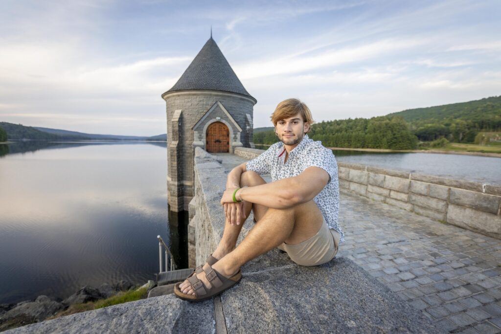 Rob Faber Photography | FBR Media | Senior Guys Portraits | Male senior sitting beside a stone tower overlooking the water during a cinematic outdoor portrait session in Simsbury Connecticut