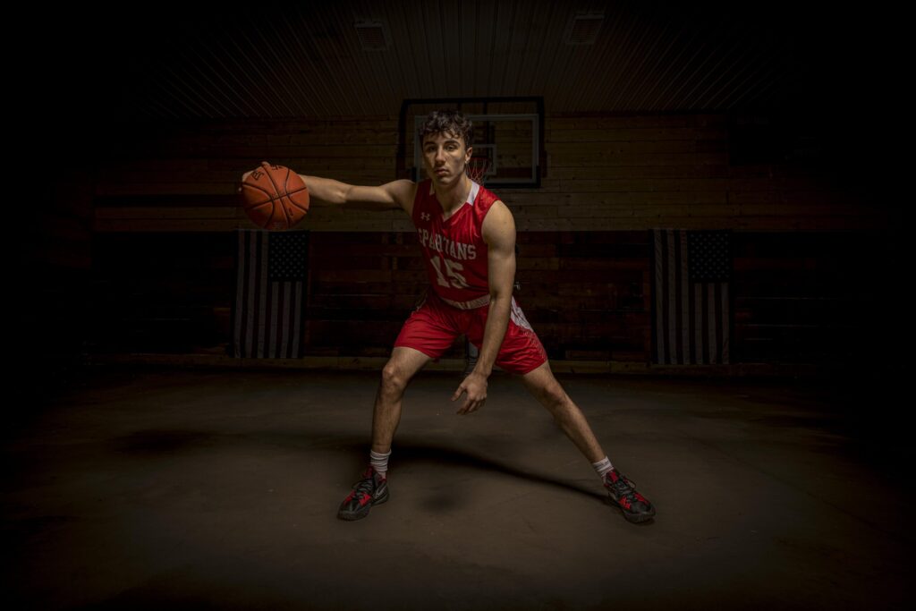 Rob Faber Photography | FBR Media | Senior Guys Portraits | Moody basketball portrait of a varsity athlete in a defensive stance on a dark gym court with dramatic sports lighting
