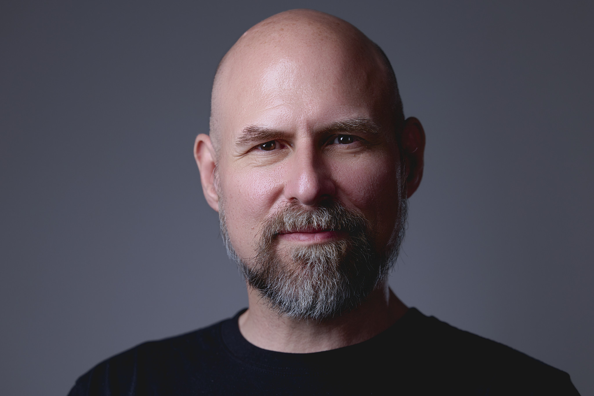 CT Headshots | Rob Faber Photography | Peter Hurley Headshot Intensive | Bald man with a full gray beard wearing a black t-shirt, calm approachable expression against a gray background.