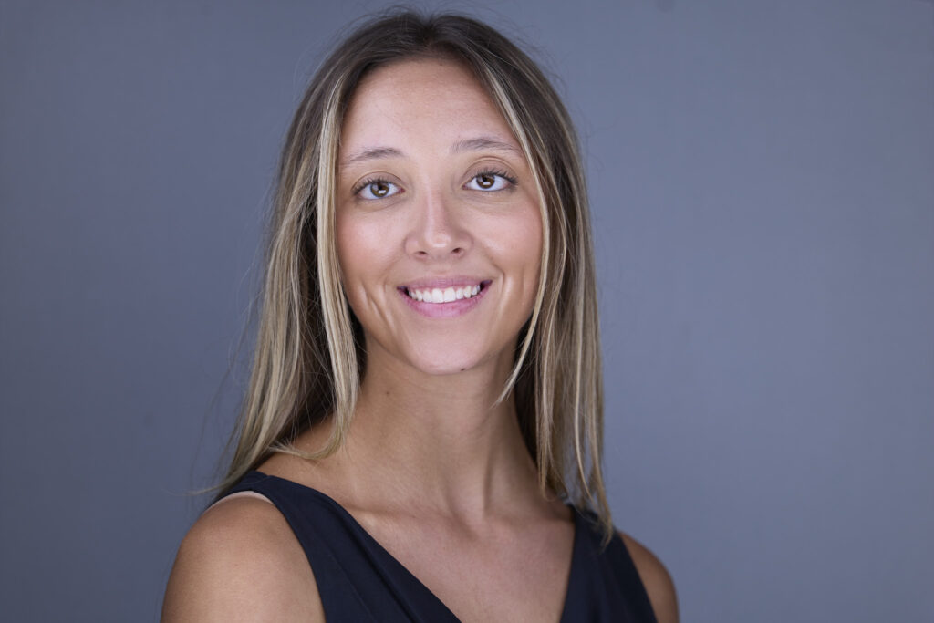 CT Headshots | Rob Faber Photography | Peter Hurley Headshot Intensive | Woman with long blonde-highlighted hair wearing a black sleeveless top, bright natural smile against a medium gray background.