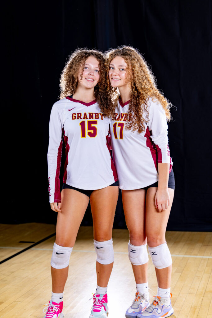 Rob Faber Photography | CT Photographer | Two Granby volleyball players with curly hair standing back to back in white and maroon long-sleeve jerseys, smiling against a dark blue studio backdrop.