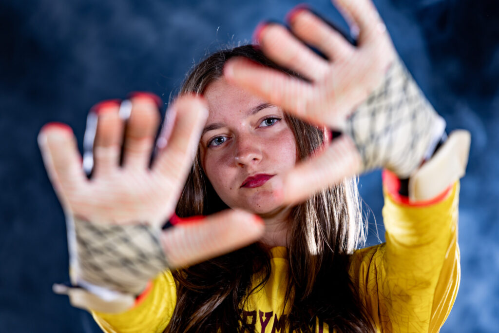 Rob Faber Photography | CT Photographer | Granby girls soccer goalkeeper in a yellow jersey framing her face with outstretched gloved hands, photographed against a smoky blue studio backdrop.