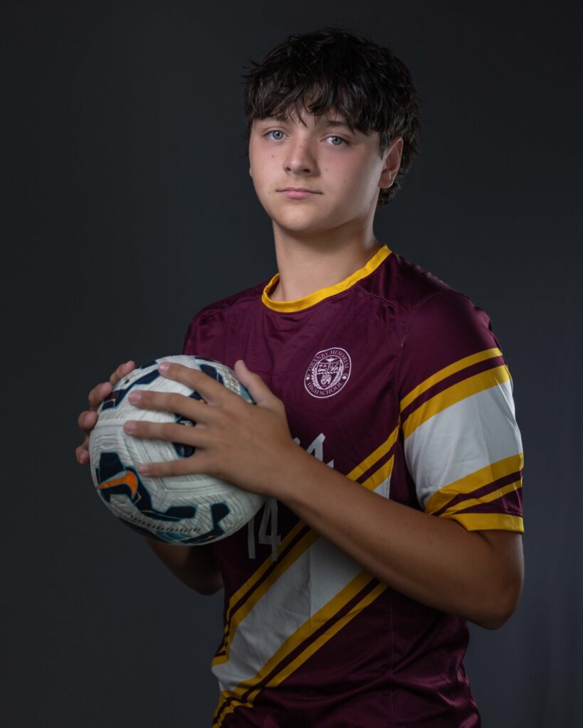 Rob Faber Photography | CT Photographer | Granby Memorial High School boys soccer player in a maroon and gold #14 jersey cradling a soccer ball in both hands, photographed against a dark studio backdrop during a sports media day session.