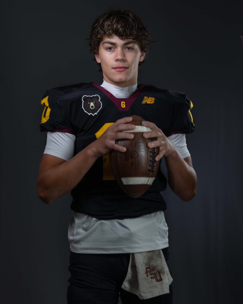 Rob Faber Photography | CT Photographer | Granby Bears football player in a black #10 jersey with a bear logo, holding a football in both hands and looking directly at the camera in a moody studio portrait.